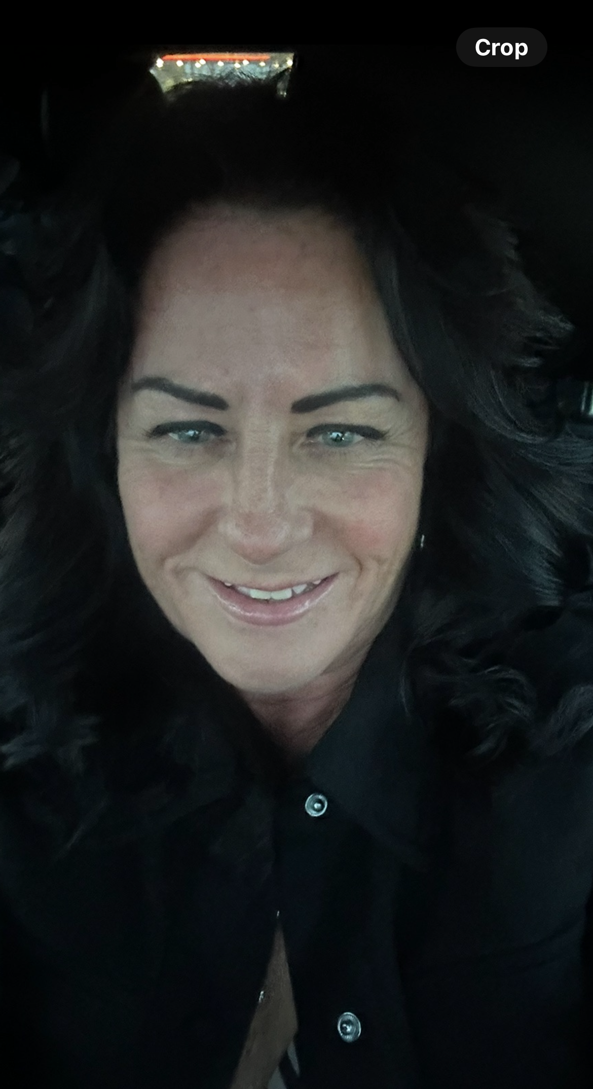 Woman with dark hair and blue eyes smiles, wearing a black shirt.