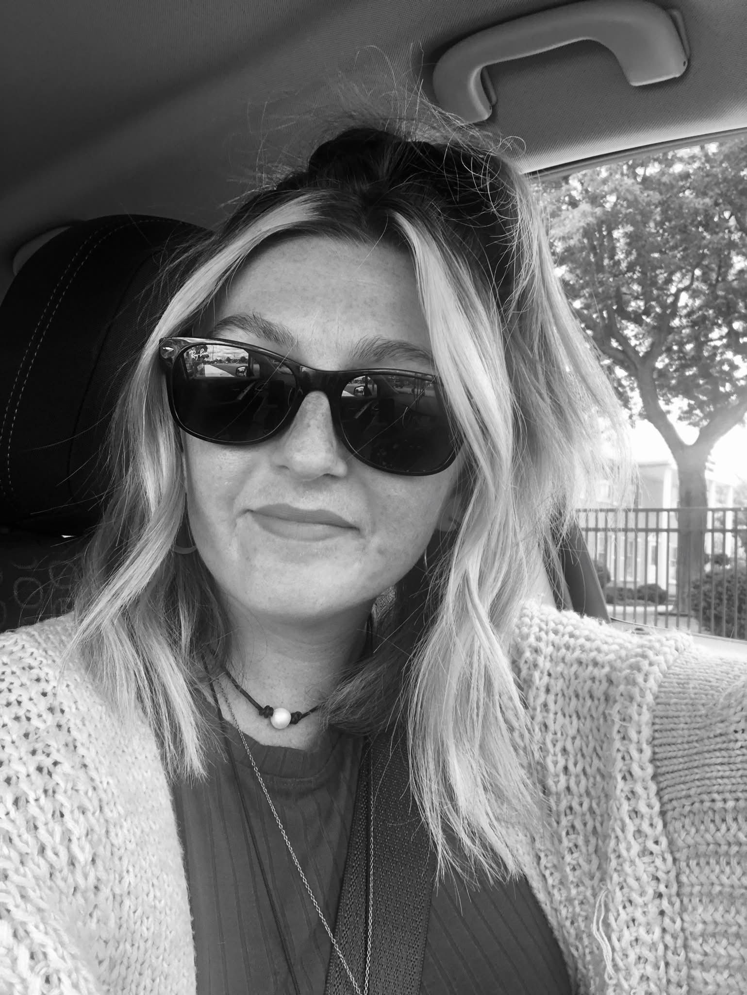 A woman wearing sunglasses and a sweater is sitting in a car.