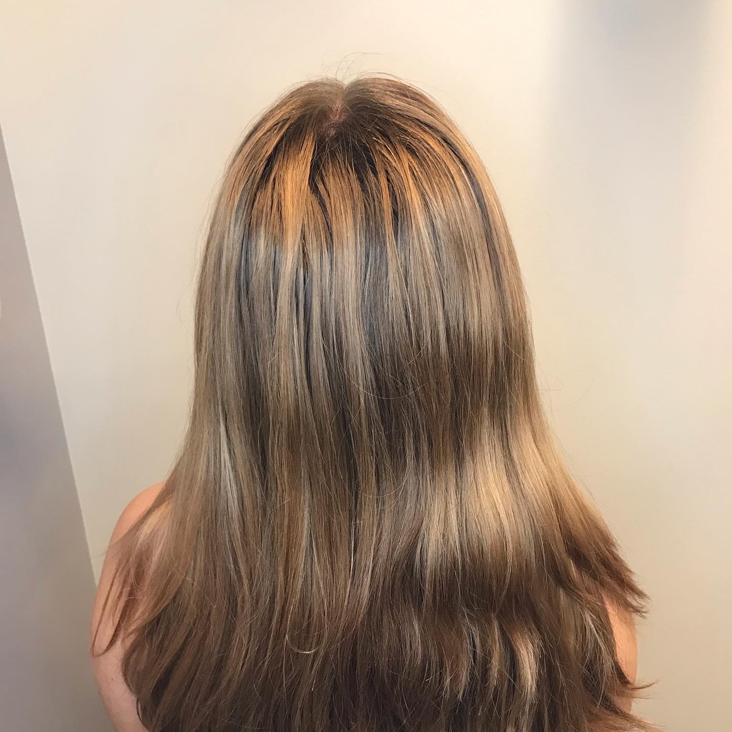 A woman with long brown hair is standing in front of a white wall.