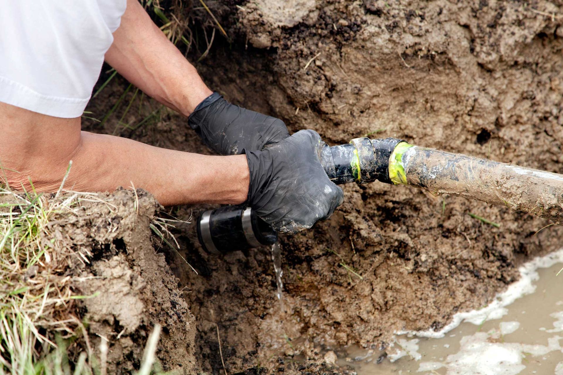 A man is fixing a pipe in the mud.