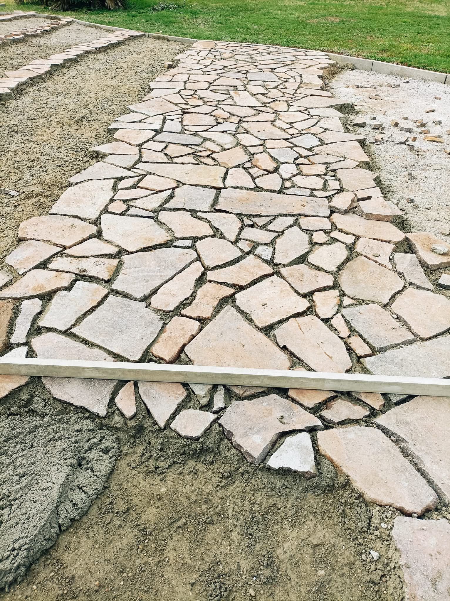 Percorso lastricato in costruzione. Pezzi di pietra incastonati nella ghiaia, delimitati da ghiaia grezza ed erba.