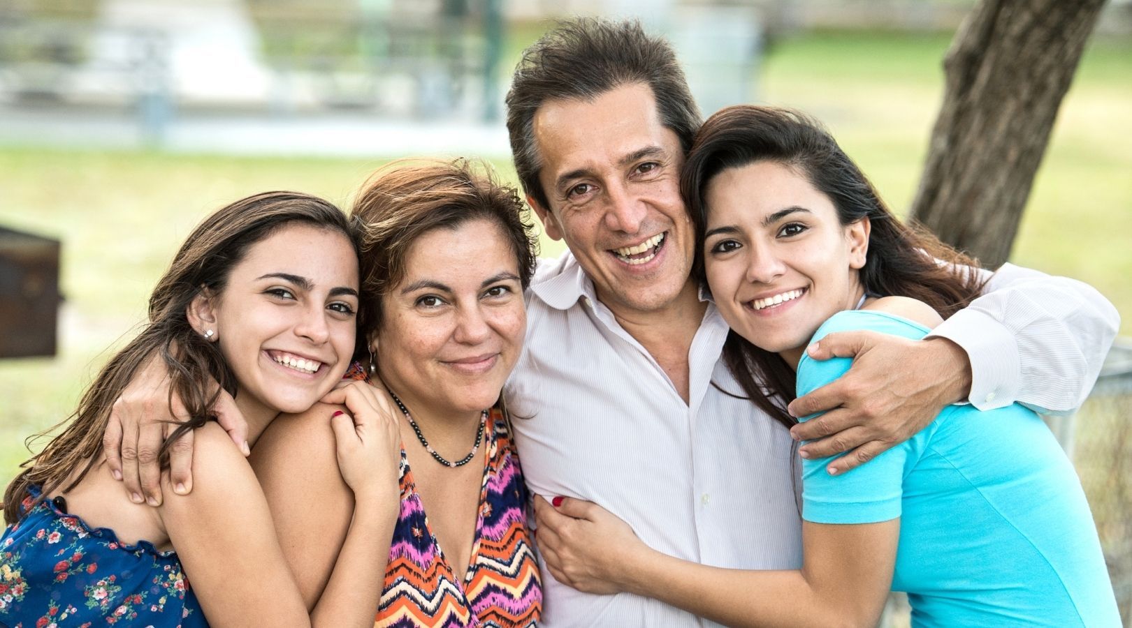 Family of four smiling and embracing outdoors.