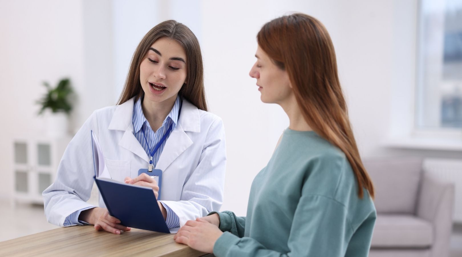 Woman in lab coat reviewing paperwork with a patient at a counter in a bright room.