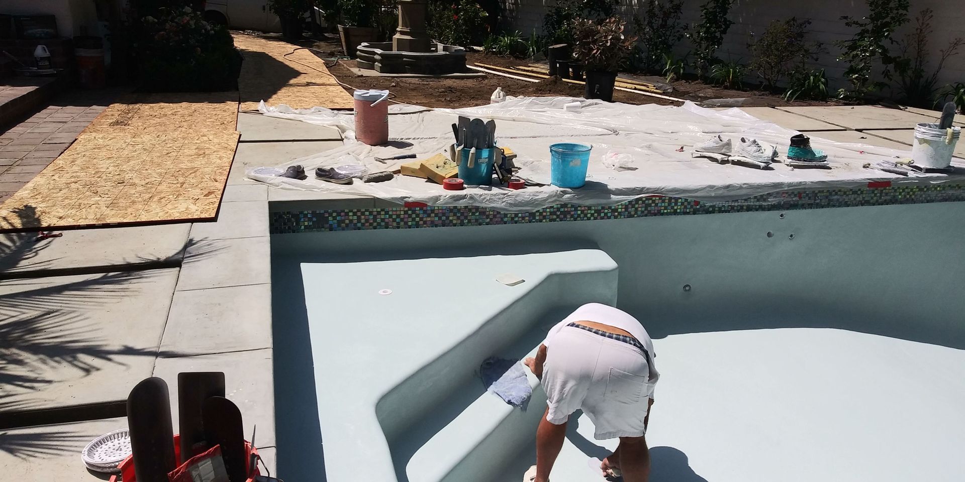 Person cleaning a pool wall with a brush beside a backyard swimming pool