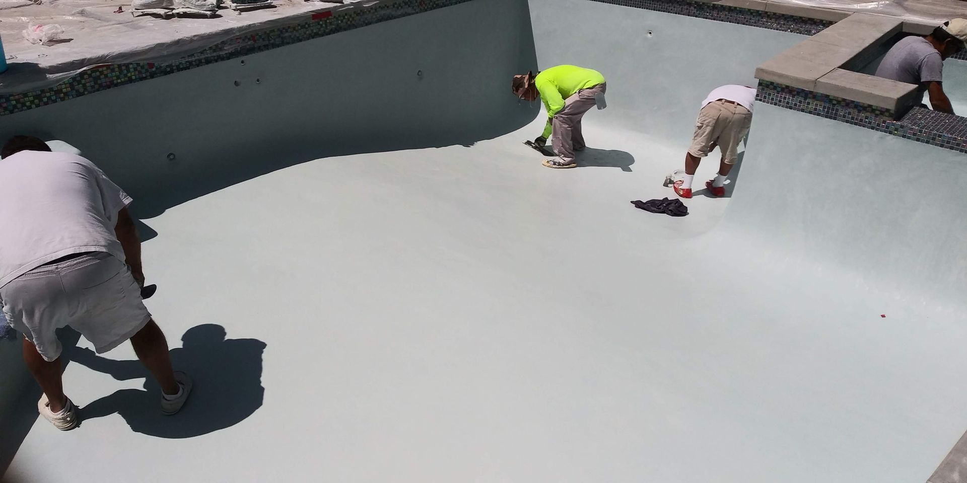 Workers installing a light gray coating on a large rooftop surface.