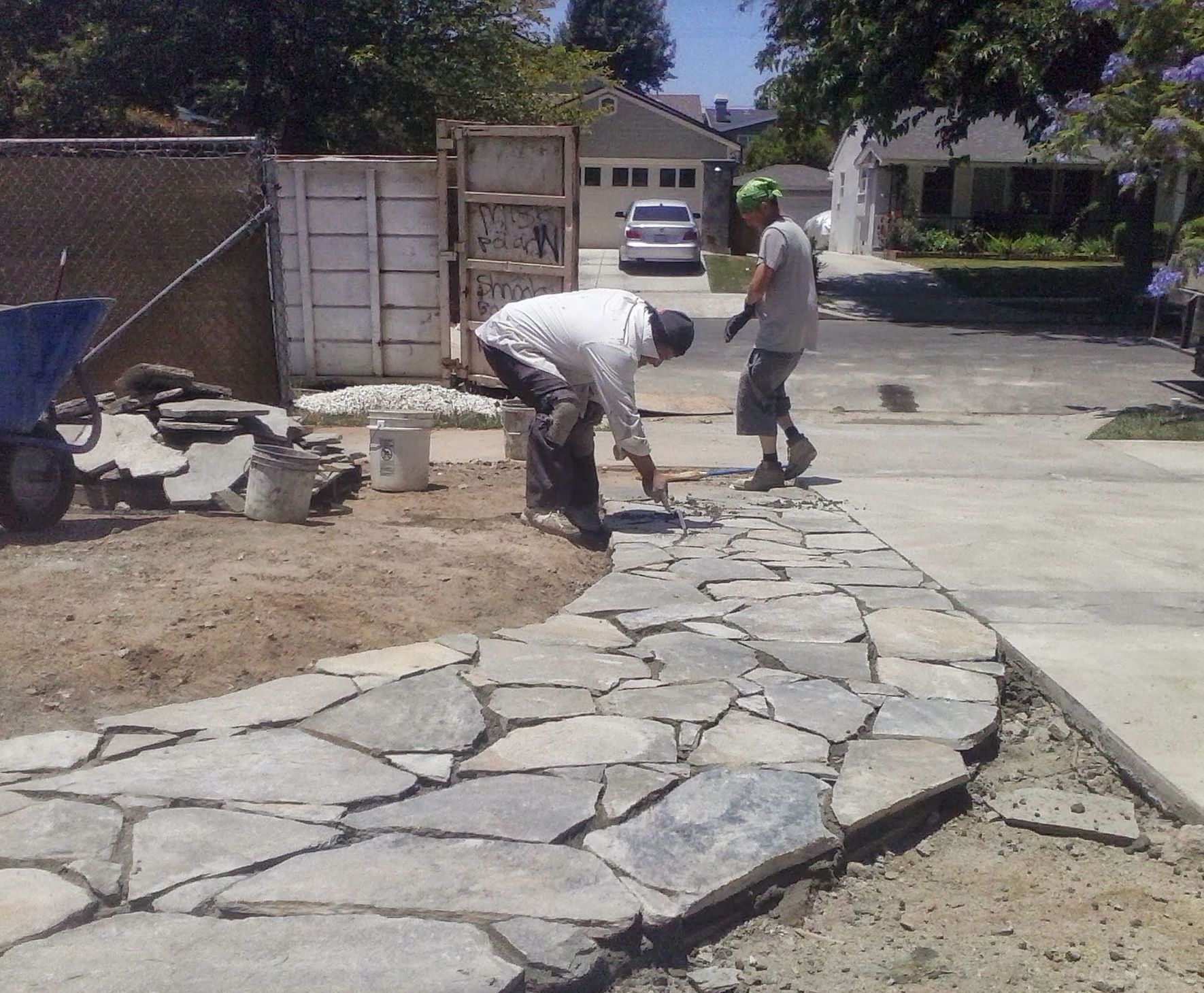 Two workers laying stone pavers along a curved walkway beside a driveway