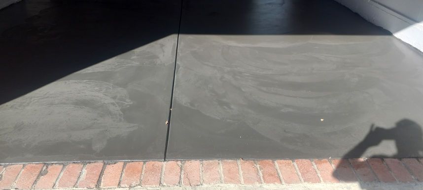 Concrete driveway with a brick border in front of a garage, with a personβs shadow in the lower right.