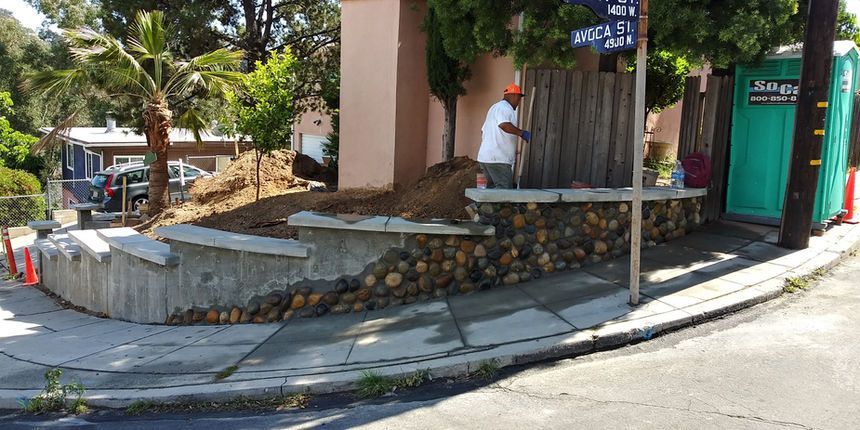 Curved sidewalk beside a stone planter wall and building entrance on a sunny street corner