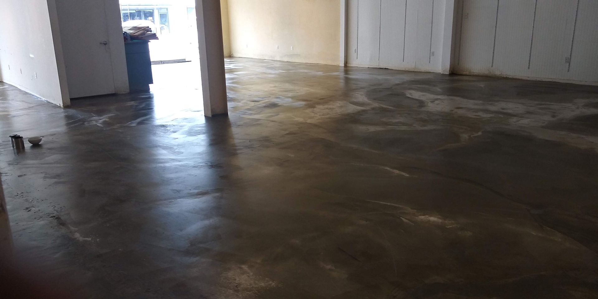 Empty indoor room with a glossy concrete floor and white walls, lit by daylight from an open doorway.