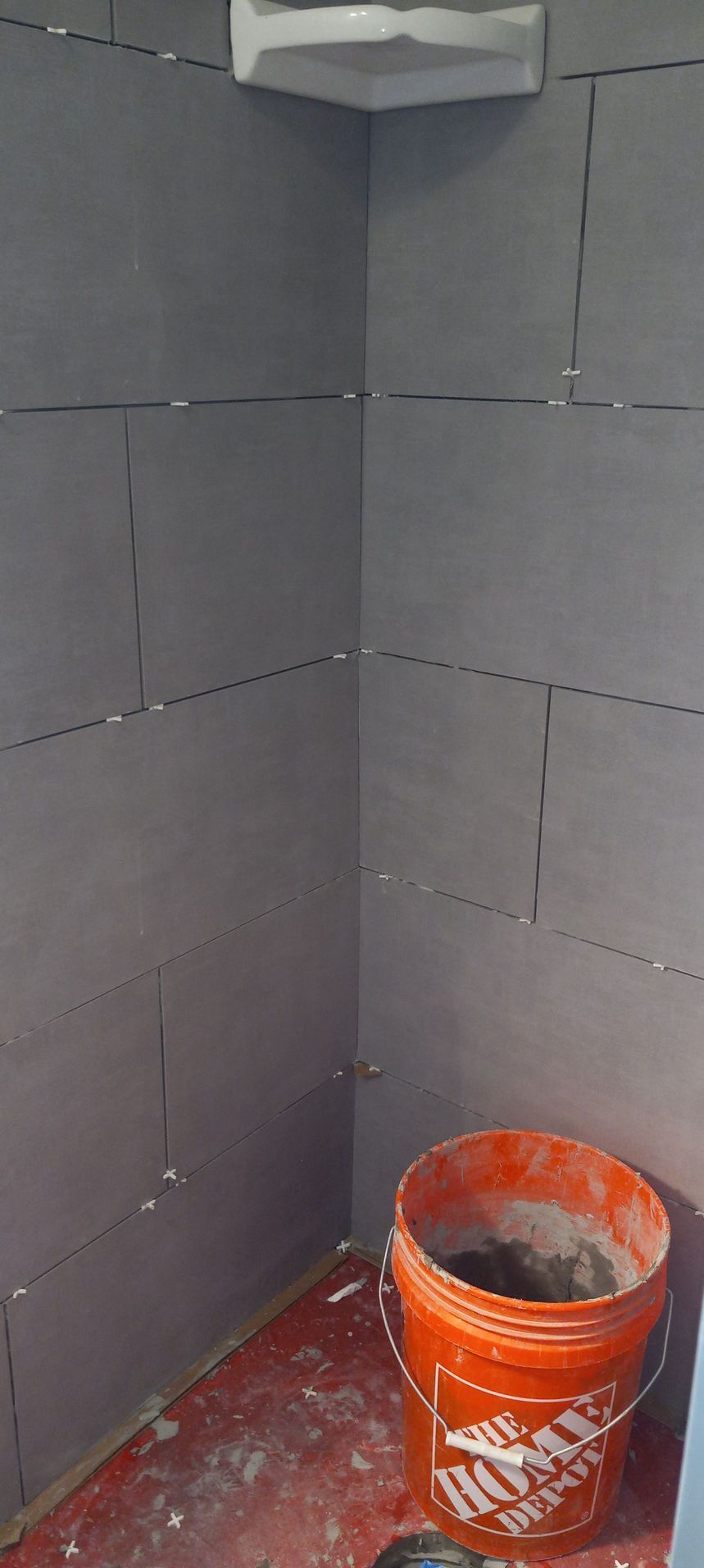 Partially tiled corner with dark gray wall panels and an orange Home Depot bucket on a red floor