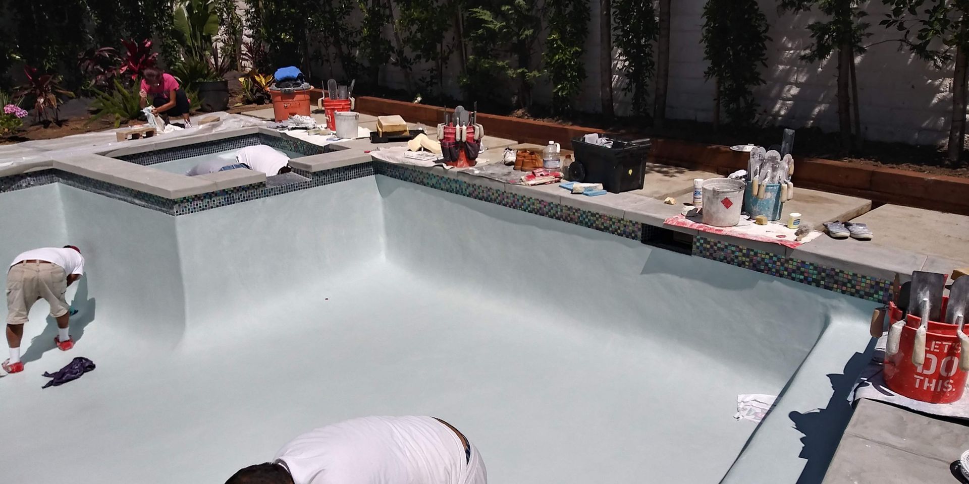 People cleaning an empty swimming pool under construction, with tools and equipment around the deck