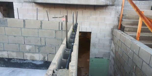 Interior construction site with cinder block walls, a narrow stair opening, and orange scaffolding railings