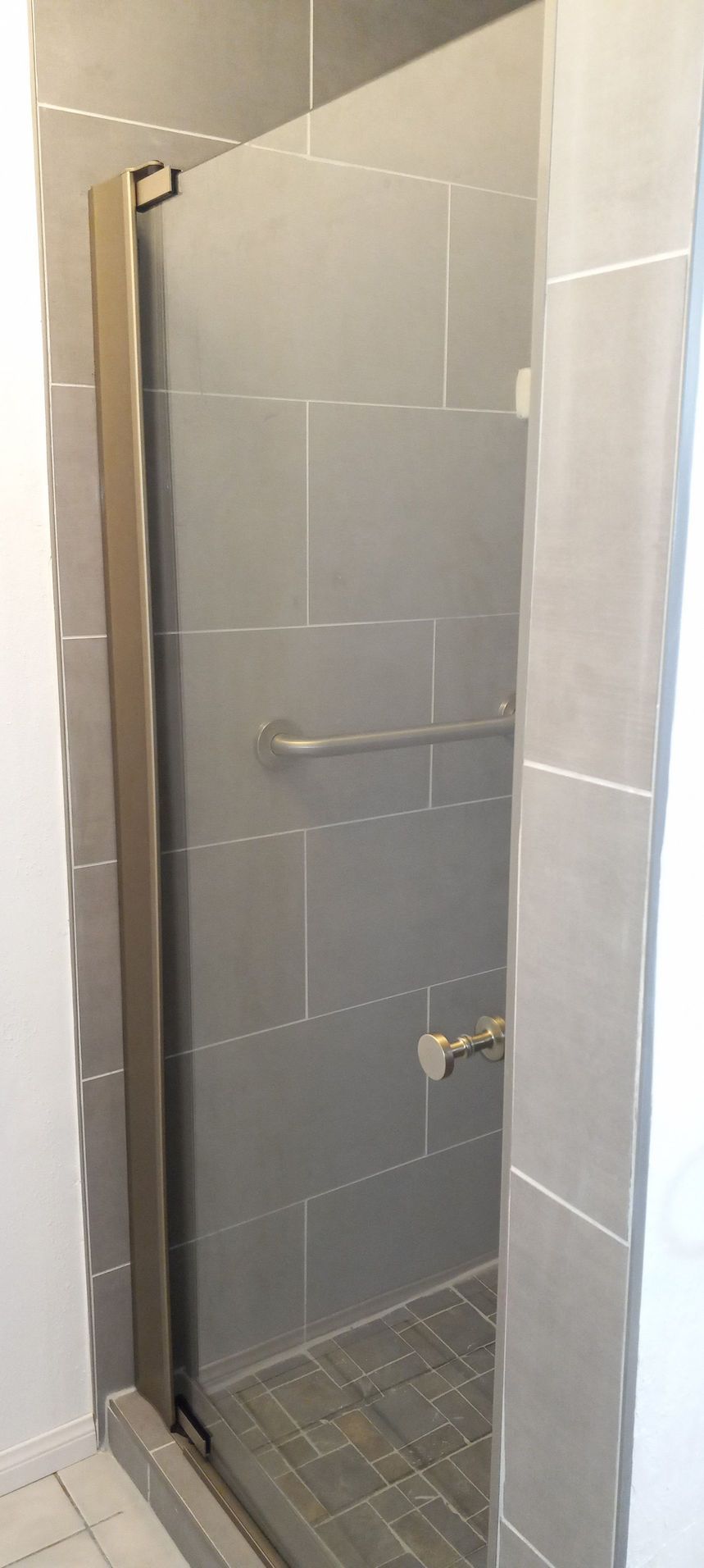 Narrow tiled shower stall with glass door and grab bars in a bathroom