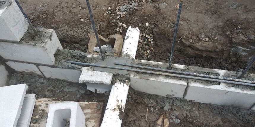 Partially built concrete wall and debris around an excavation trench with wooden planks and rebar