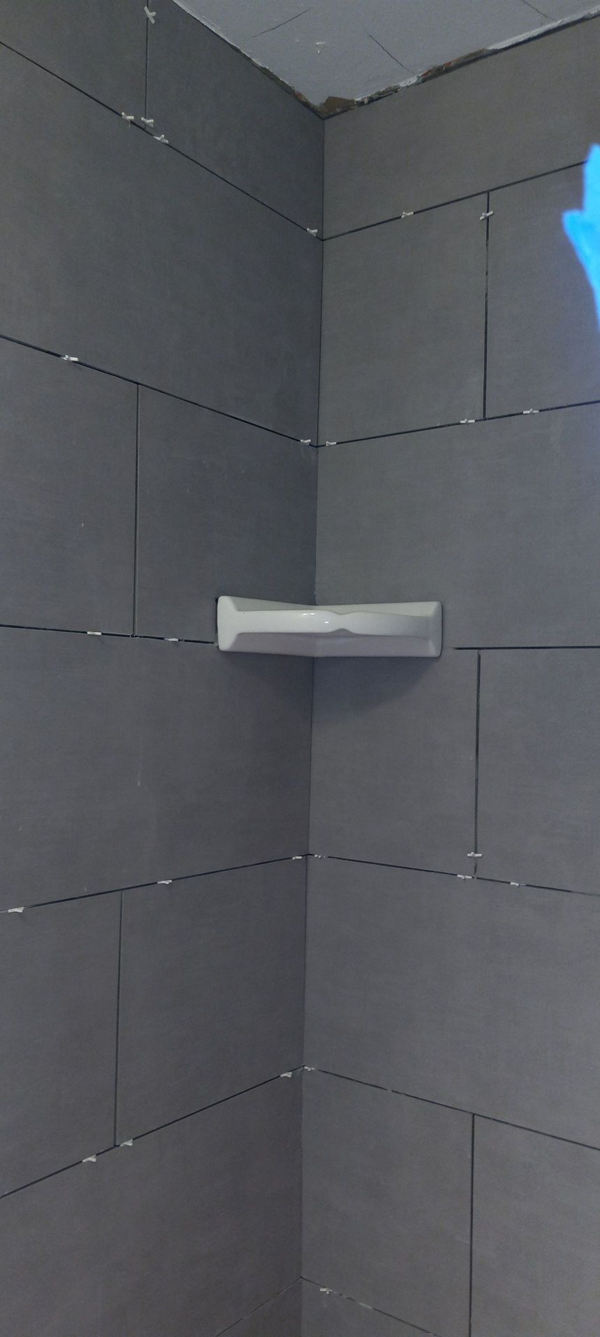 Empty gray tiled shower corner with a small white corner shelf.