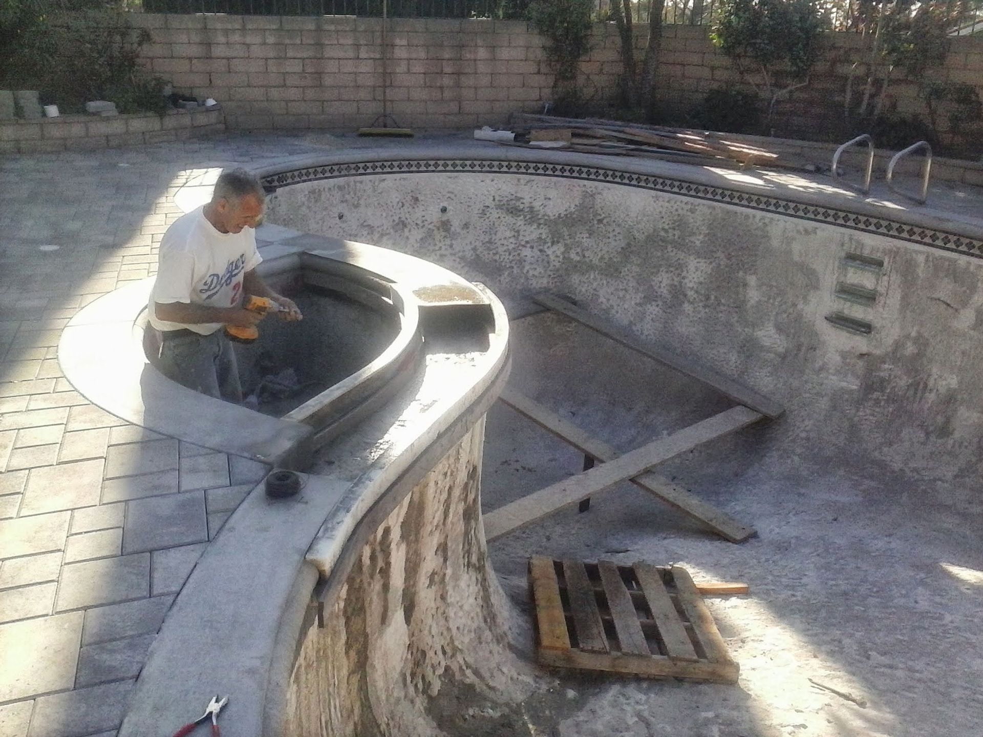 Worker repairing an empty concrete pool with curved walls and a drain grate