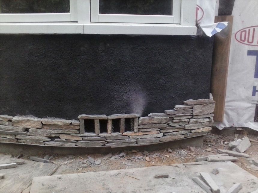 Partially finished house foundation with black stucco, stone veneer, and a row of concrete blocks