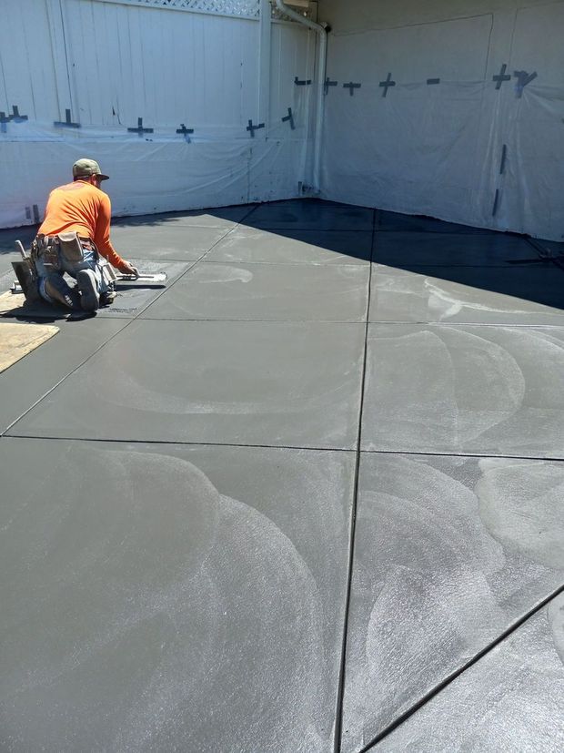 Worker in orange shirt smoothing wet concrete in a large white-walled industrial area.