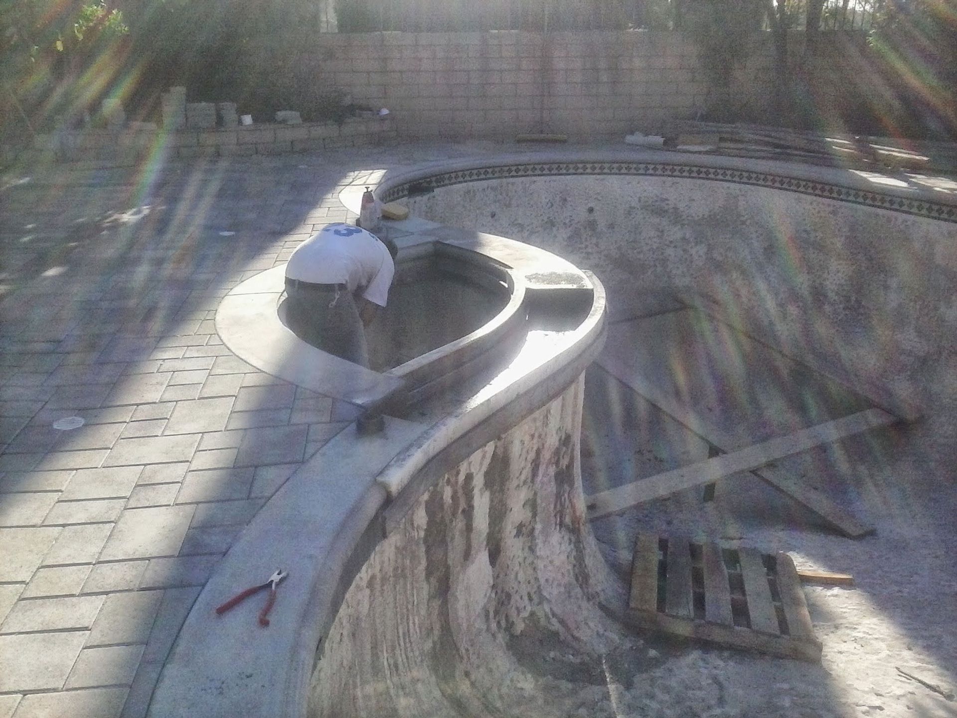 Person sitting on a curved concrete sculpture in a sunlit outdoor plaza with paving and steps.