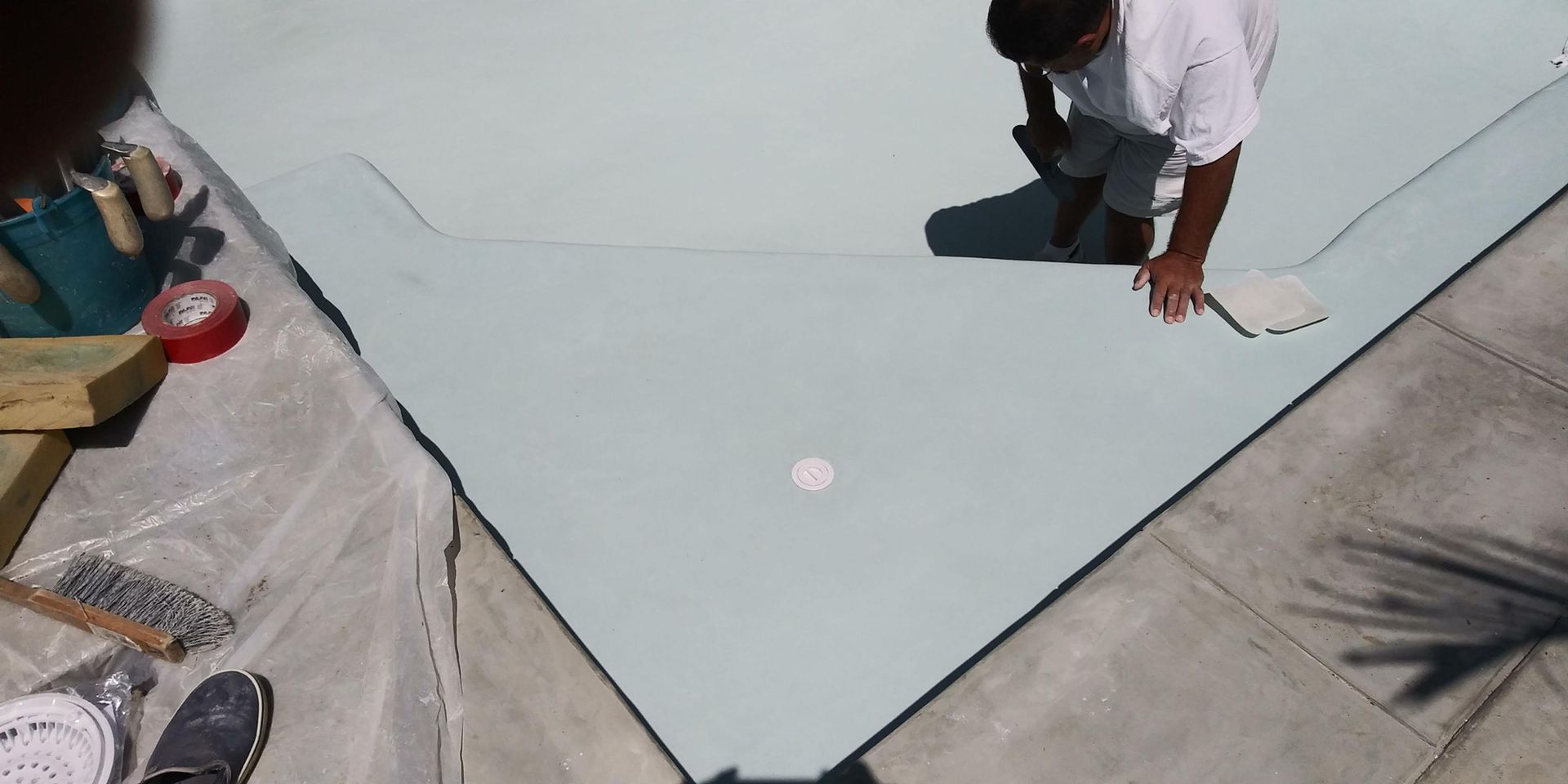 Workers applying light gray coating to a flat roof corner with paint rollers