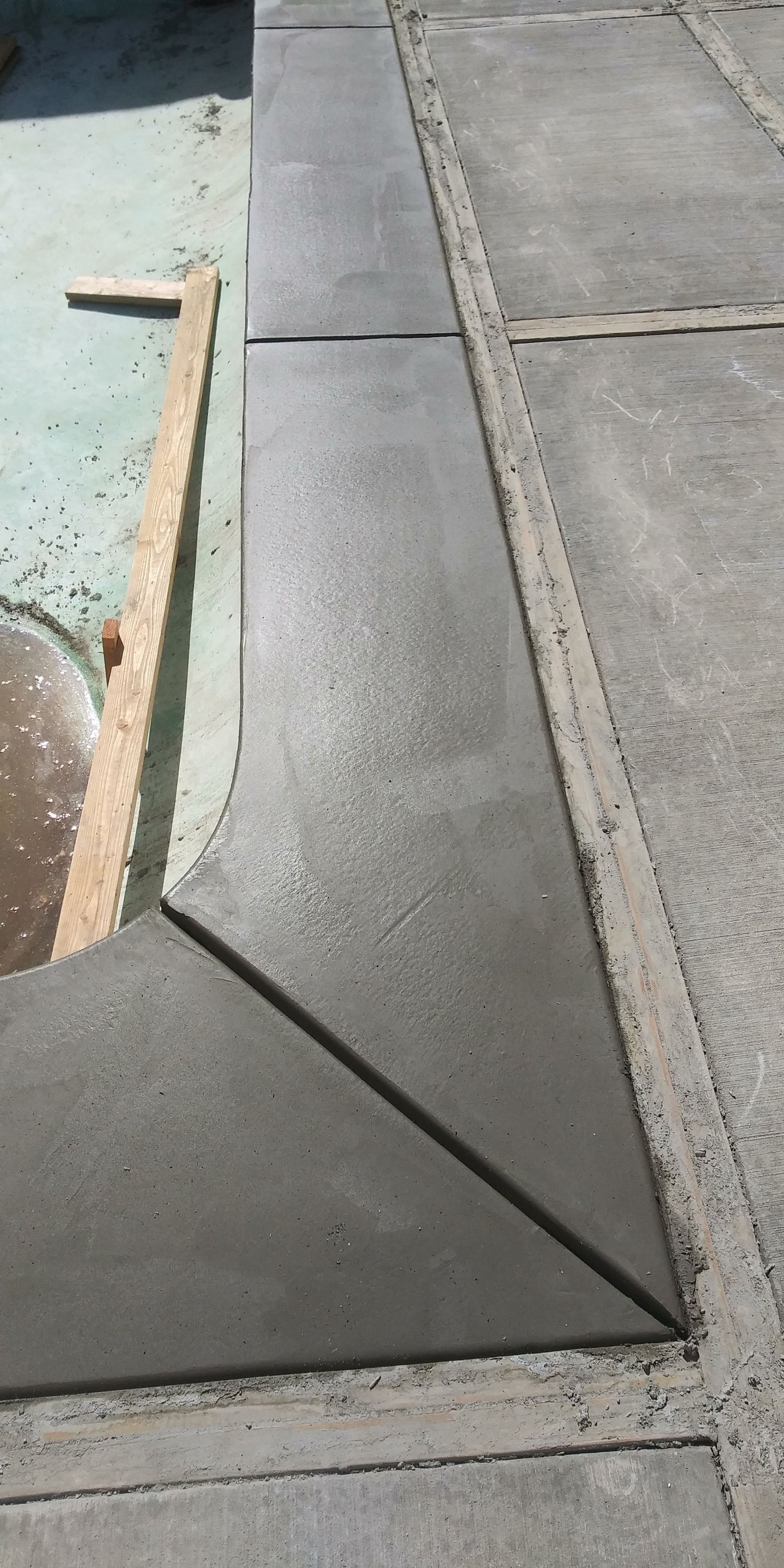 Concrete sidewalk with a triangular dark-gray patch and a raised curb edge beside a paved path