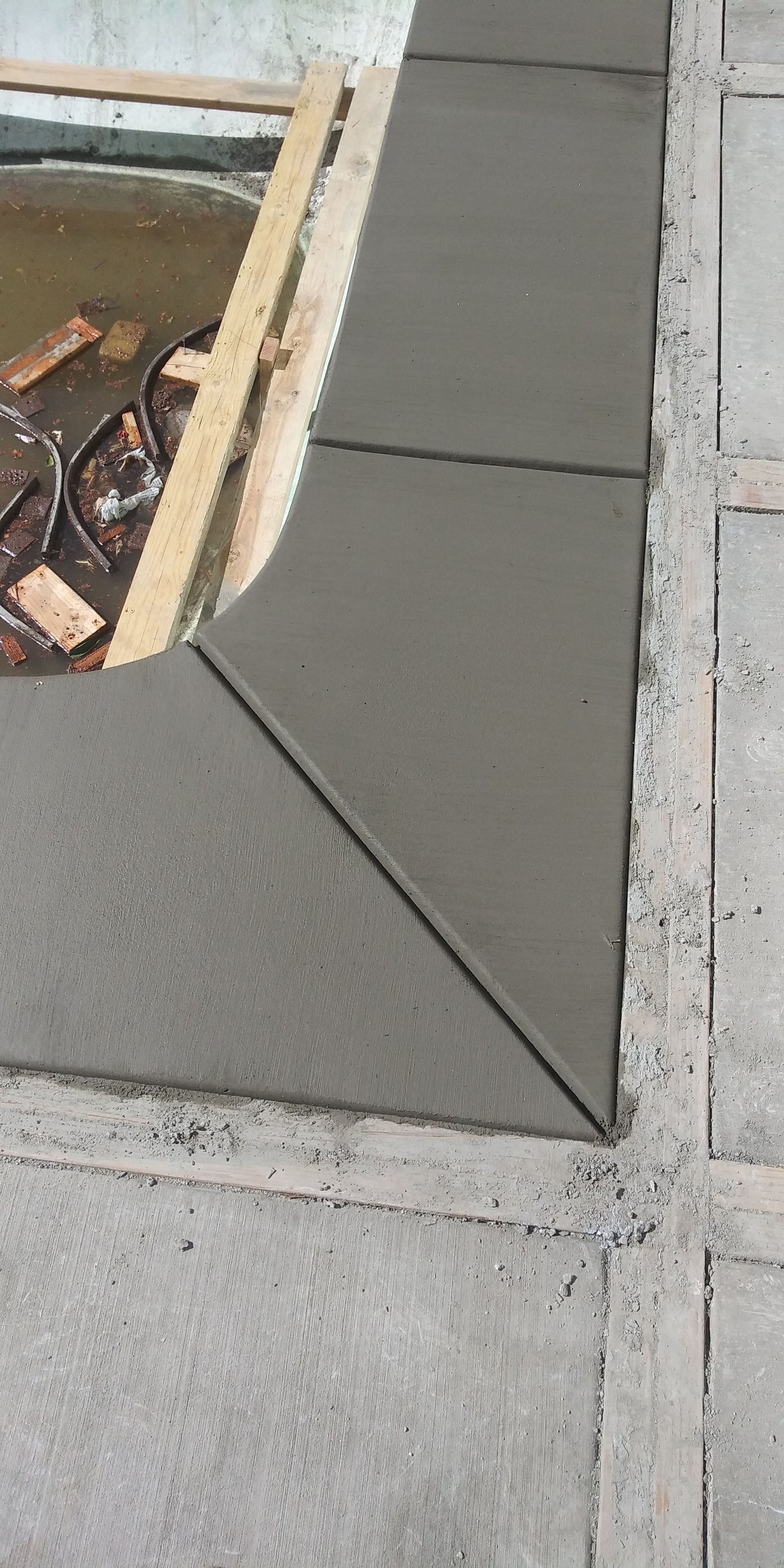 Freshly poured gray concrete walkway beside an excavation pit, with a diagonal joint line.