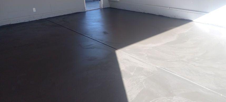 Empty indoor corner with white walls and dark floor, lit by sunlight