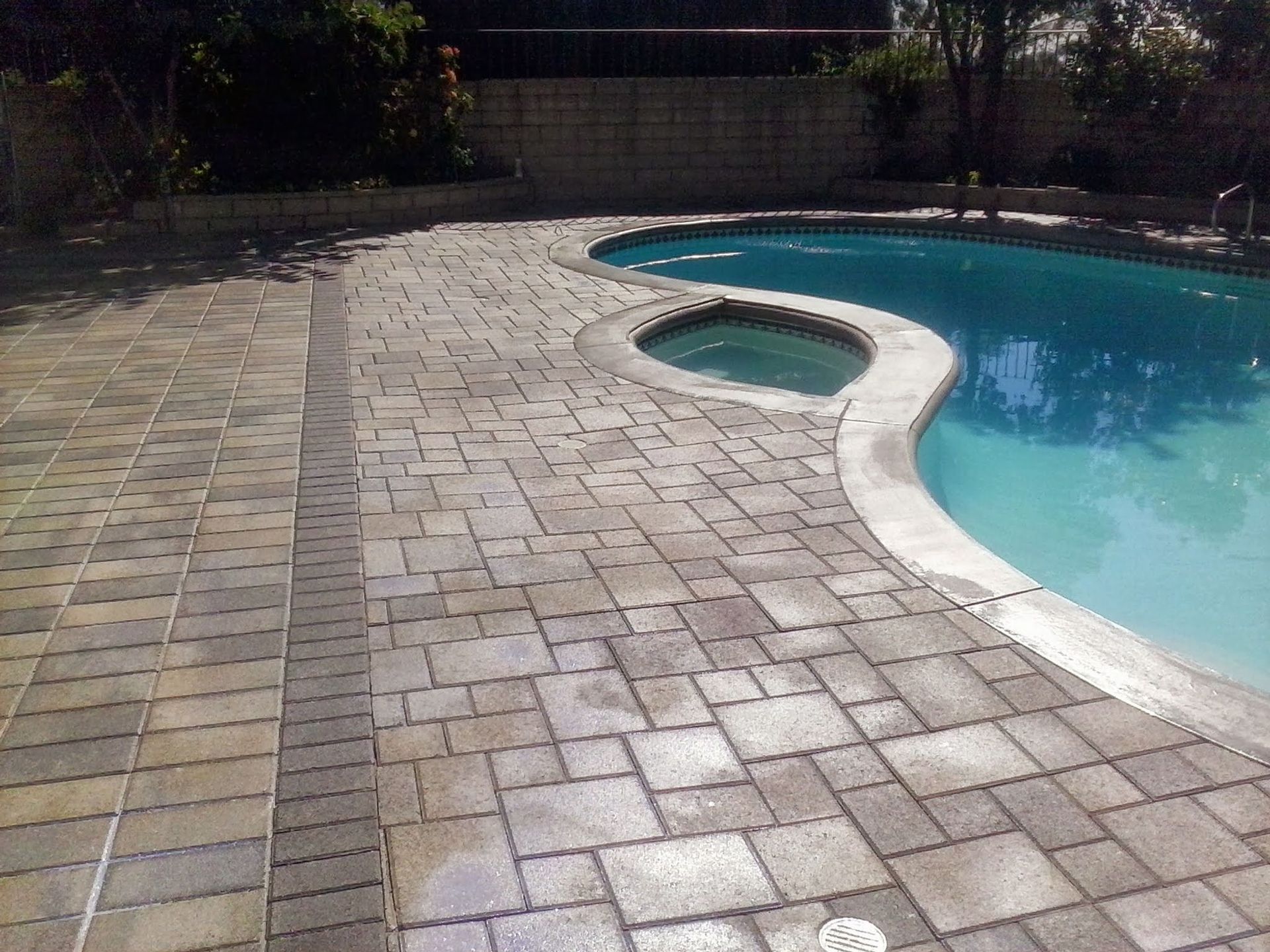 Brick pool deck with a small circular hot tub beside a turquoise swimming pool.