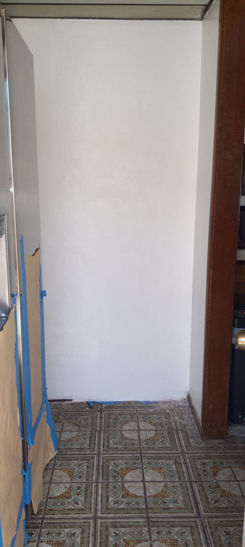 Narrow hallway with a plain white door or partition and patterned tile floor.