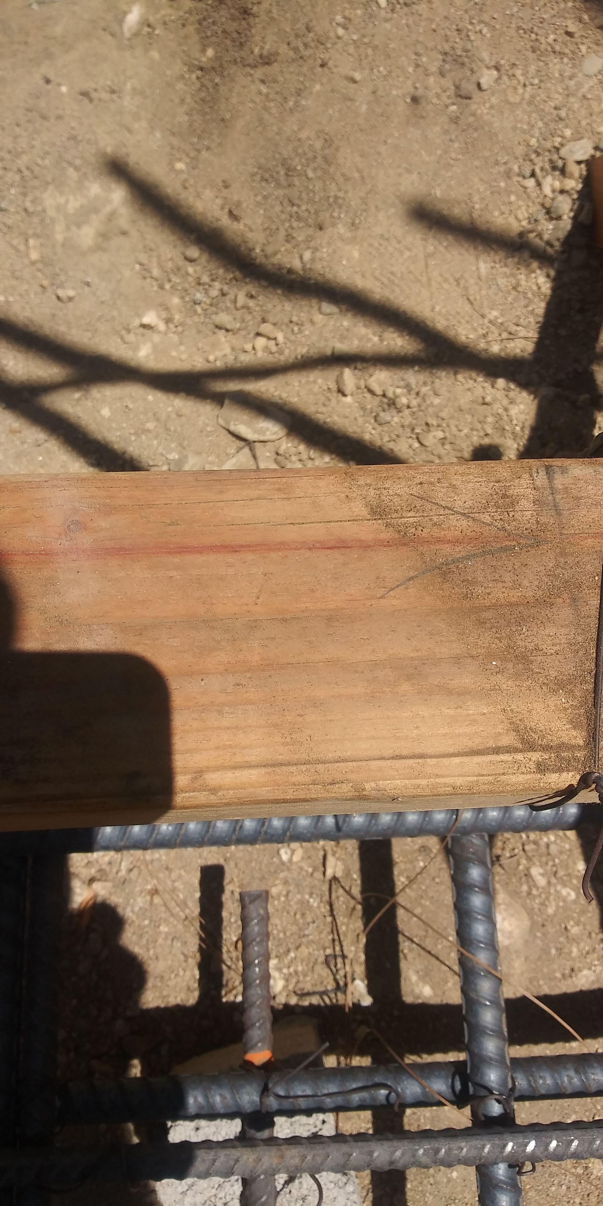 Wooden plank on a rusty metal frame outdoors, with shadows cast on a concrete surface.