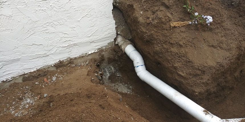 White wall corner with exposed dirt and a white PVC pipe running along the ground