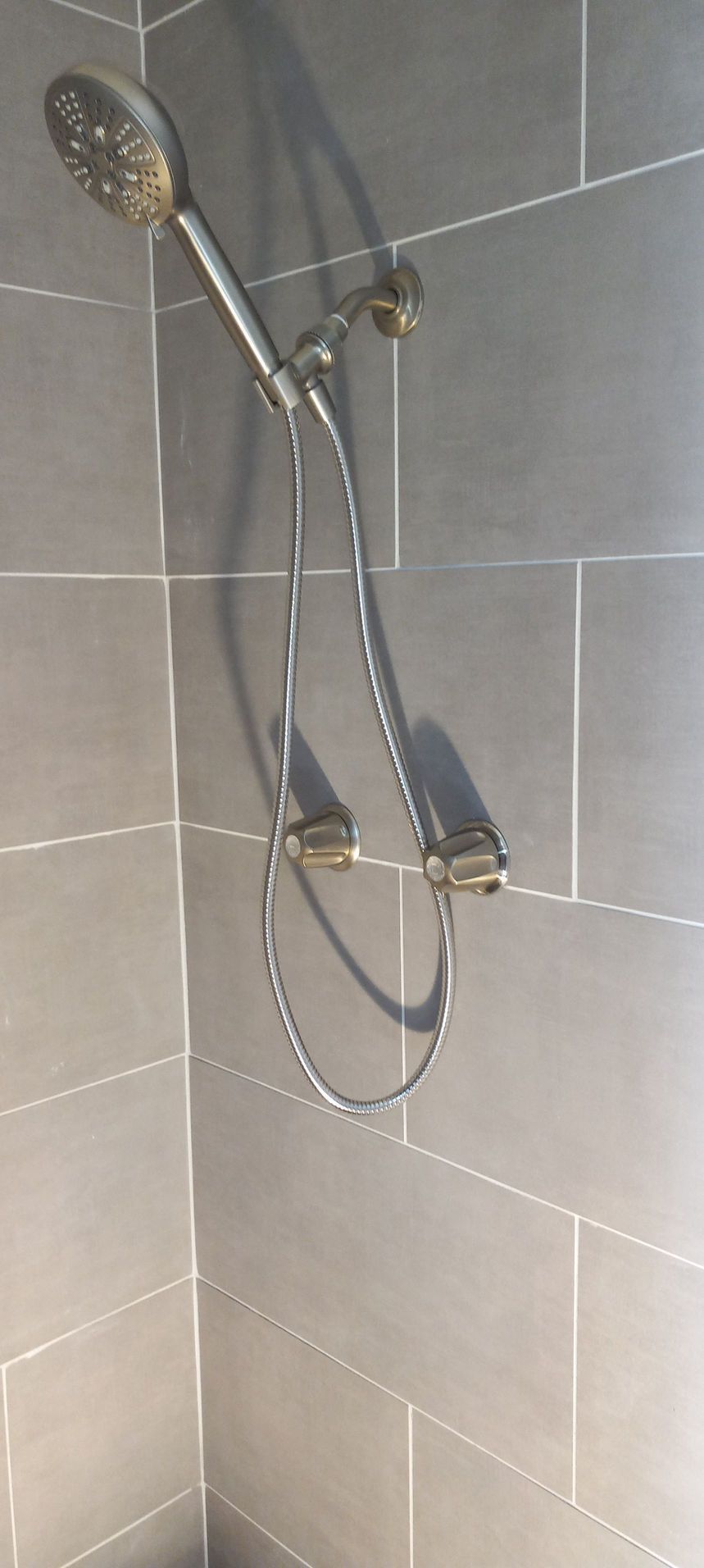 Chrome showerhead and handheld shower sprayer mounted on gray tiled bathroom wall