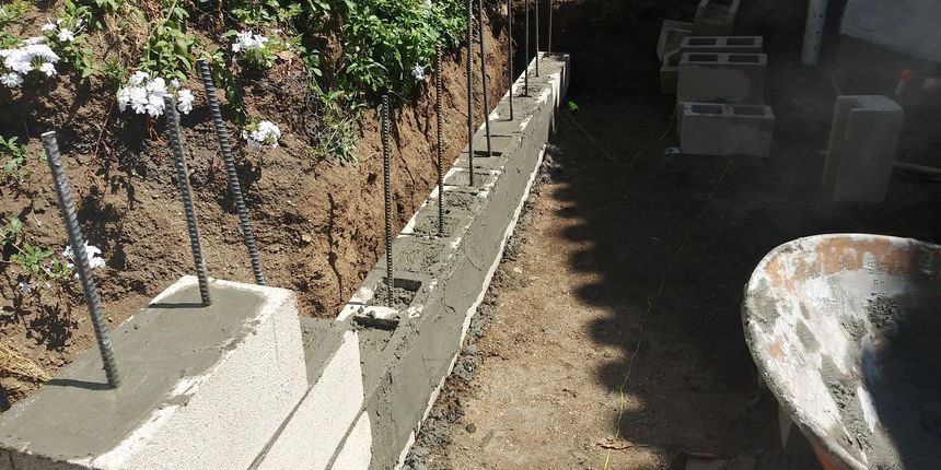 Narrow concrete walkway beside a planted dirt slope, with shadows and a rusty tub on the right.
