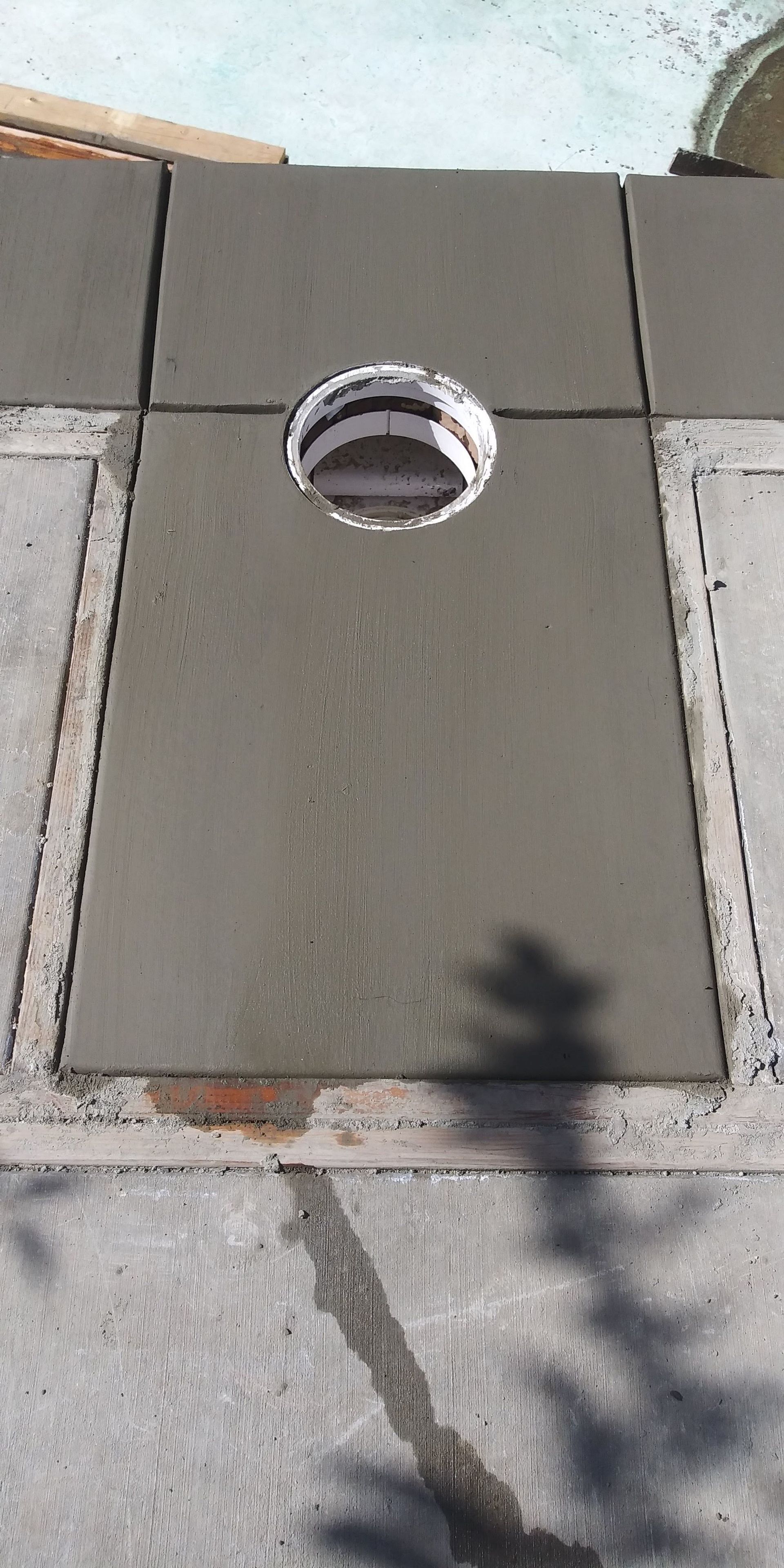 Round metal pipe opening in a gray concrete slab with pavement around it