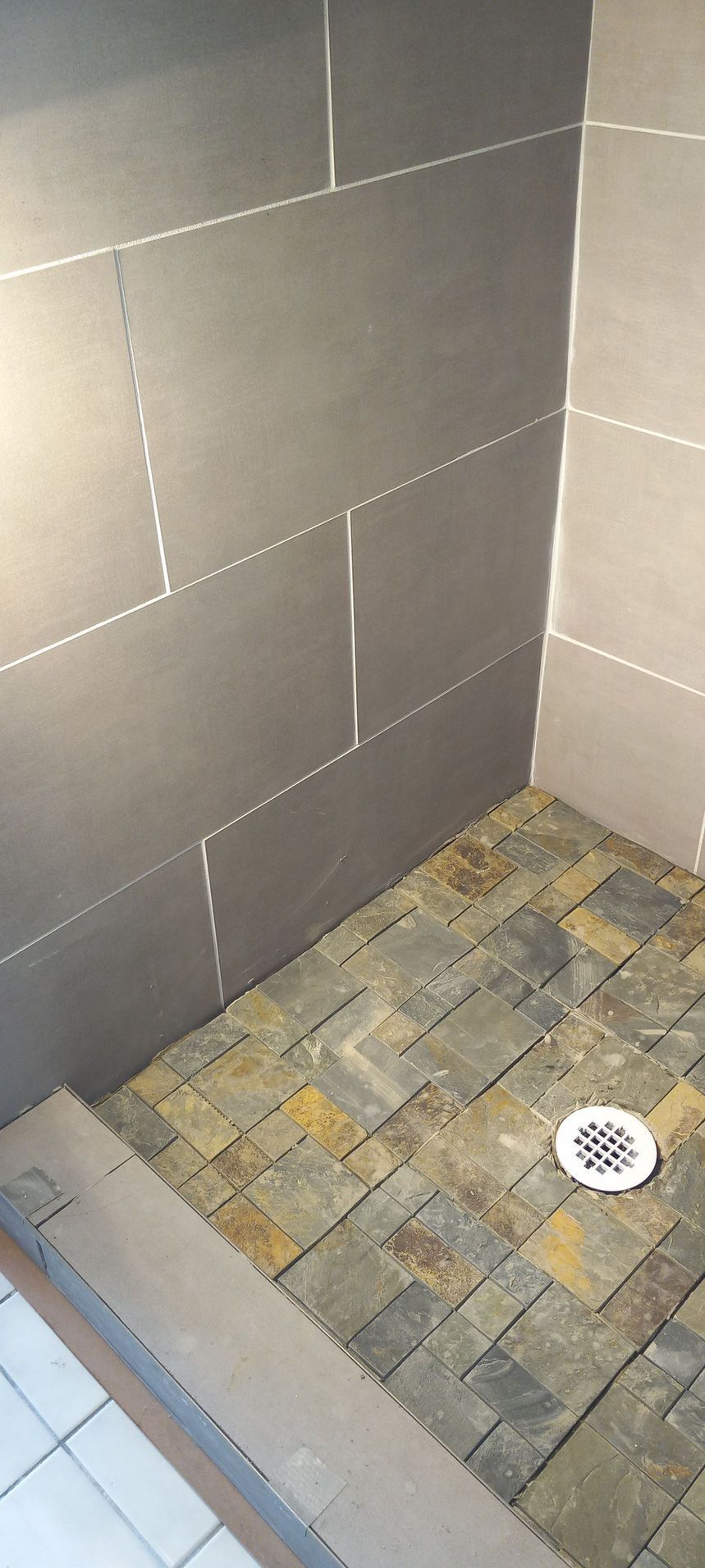 Small tiled shower corner with gray walls, mosaic floor, and a drain.