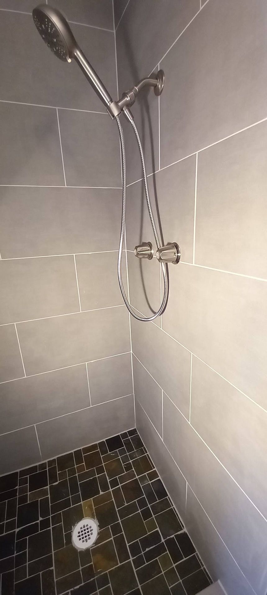 Tile shower with chrome handheld showerhead and dark mosaic floor drain.