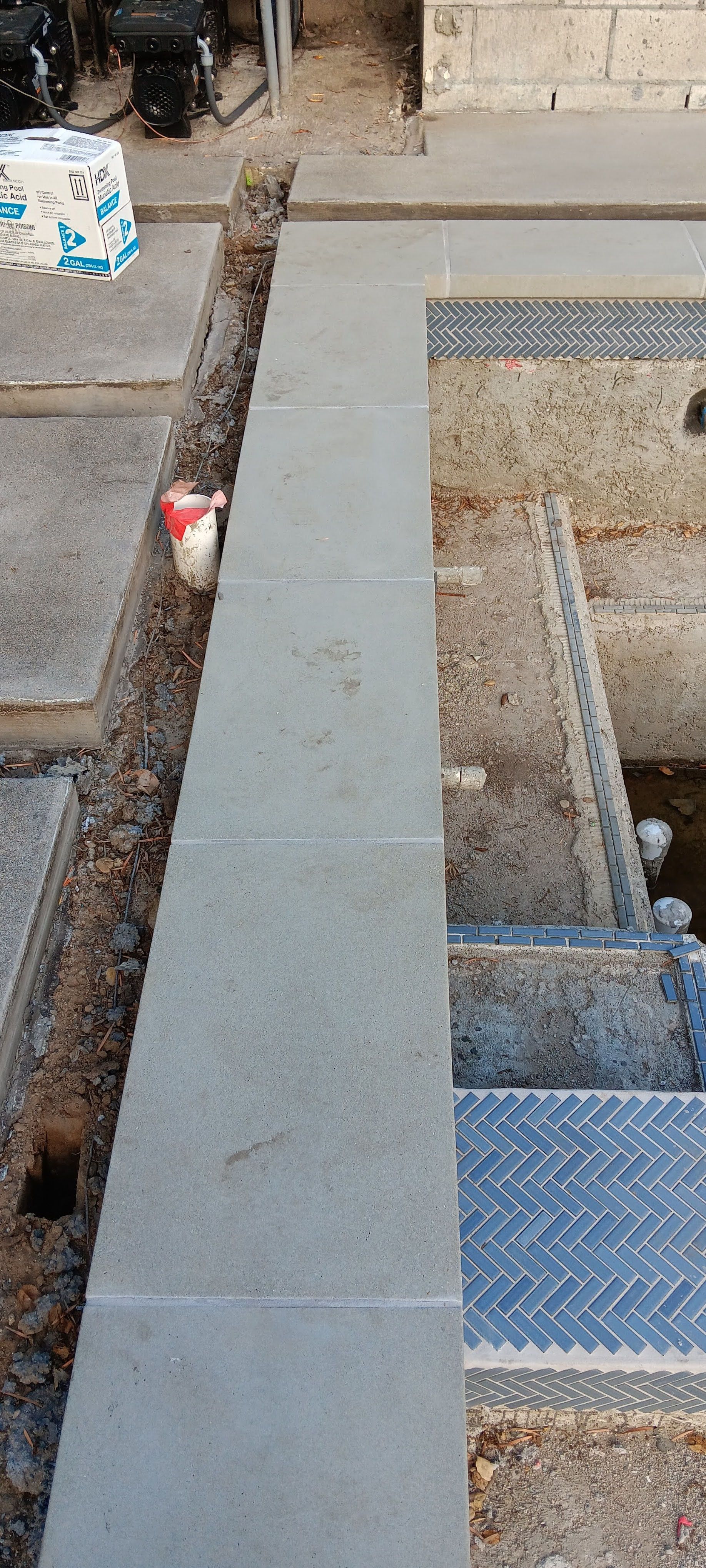 Concrete walkway beside an open trench with metal steps and a diamond-plate cover in a construction area
