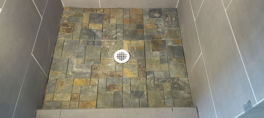 Small tiled shower floor with a central drain and gray wall tiles.