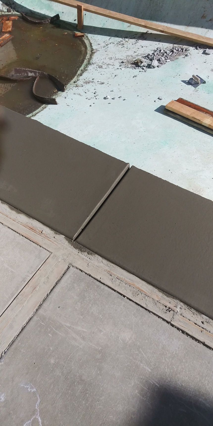 Tiled patio beside a blue pool with square gray pavers and a brown chair edge in the corner