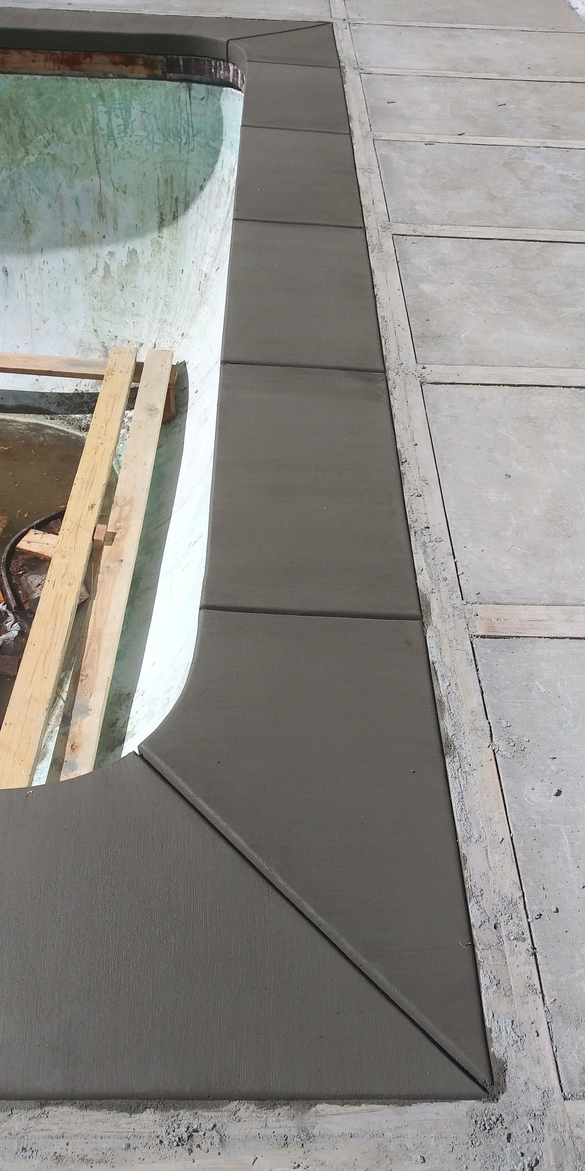 Gray sidewalk tiles beside a white planter with wooden slats and a stone curb.