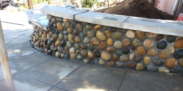 Stone retaining wall with rounded rocks and a white cap beside a paved walkway.