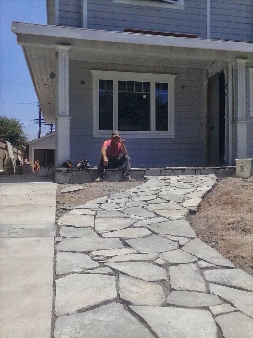 Stone walkway leading to a house entrance, with a person sitting near the porch.
