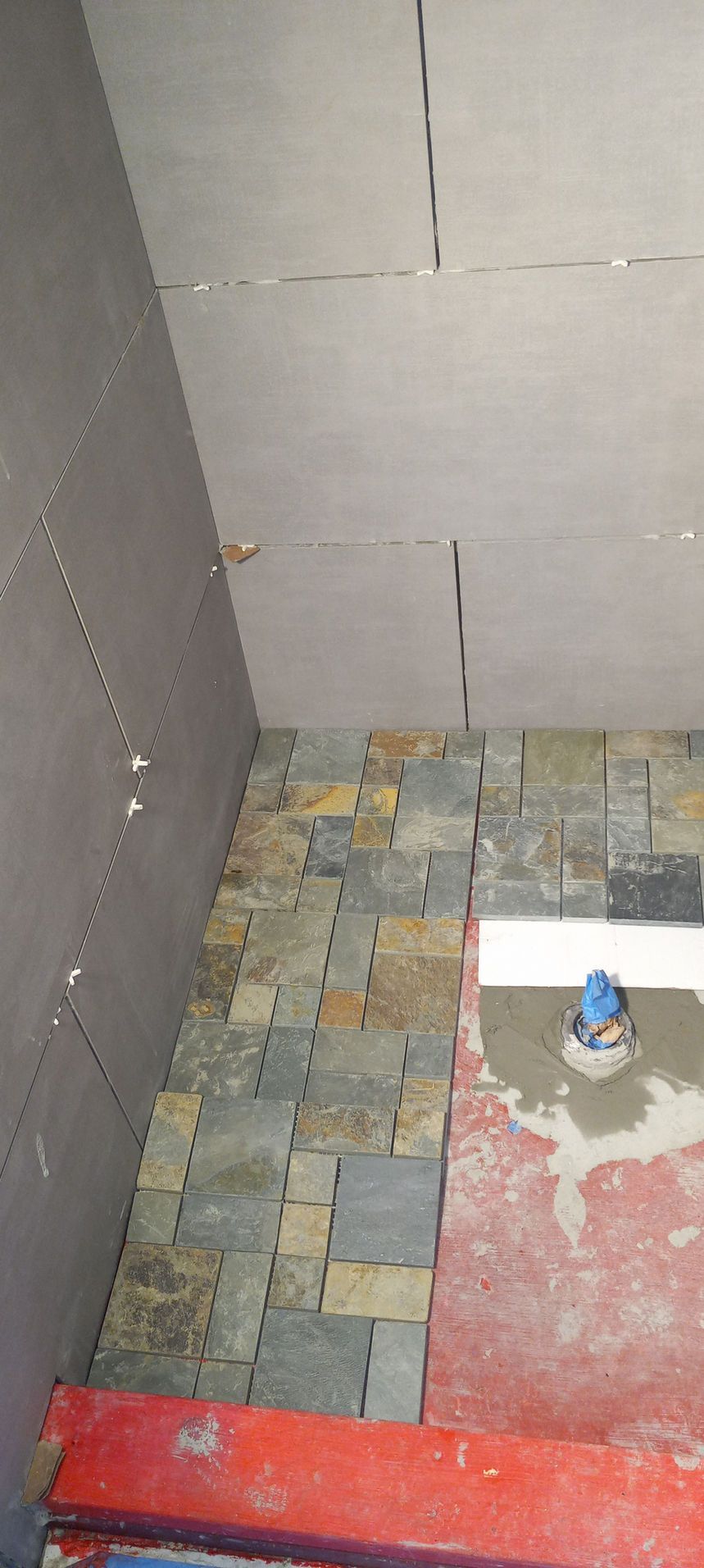 Small unfinished bathroom with tiled walls, patchy floor, and a red threshold strip near the entrance