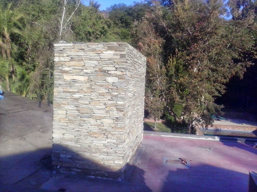 Stone pillar on a paved outdoor path beside trees and a hillside at dusk