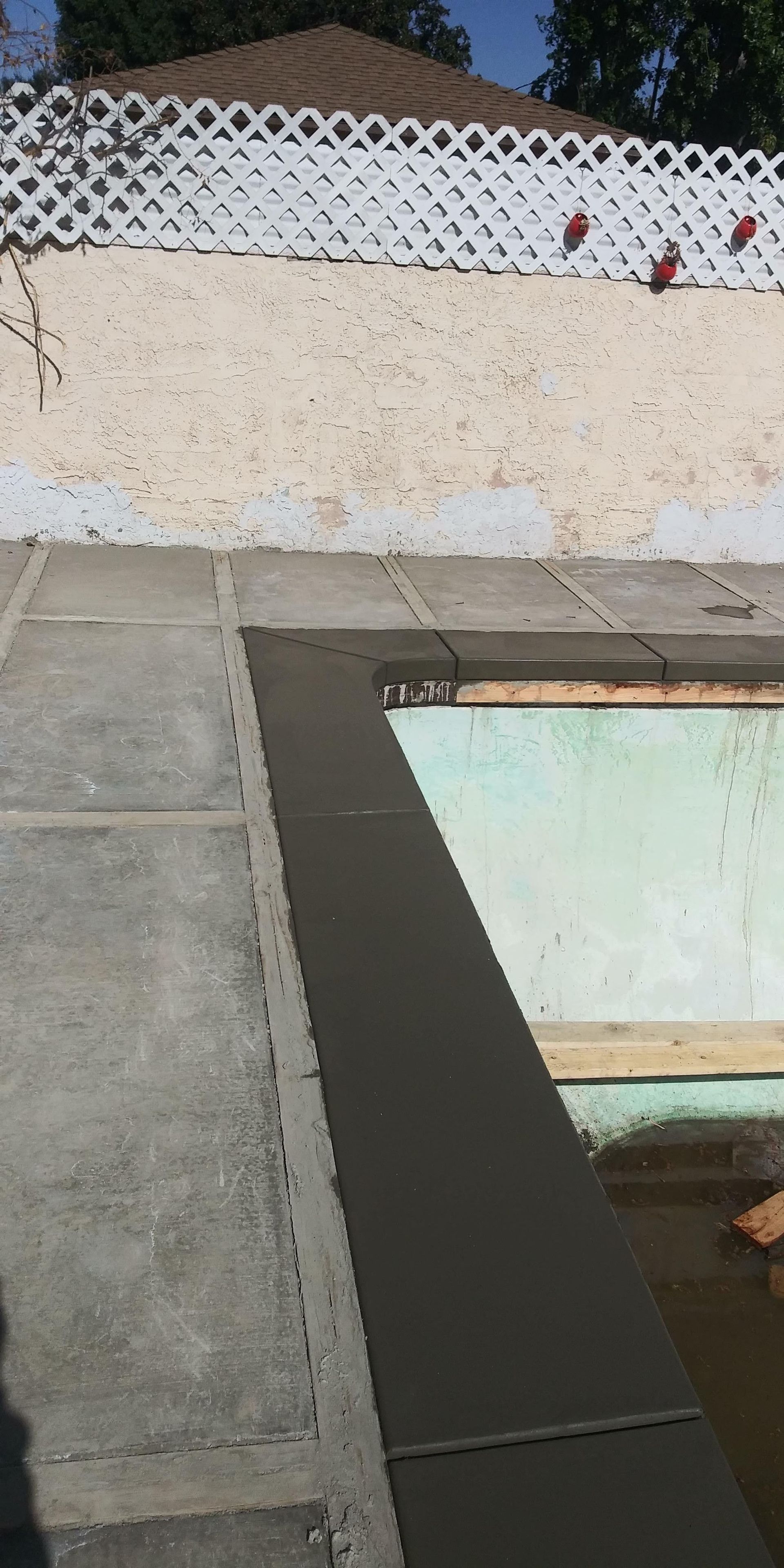 Outdoor pool deck with concrete walkway, low wall, and white lattice fence in the background