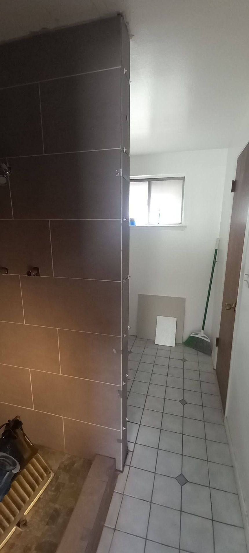 Narrow tiled hallway with a dark brown tiled wall, small window, and an open doorway at the end