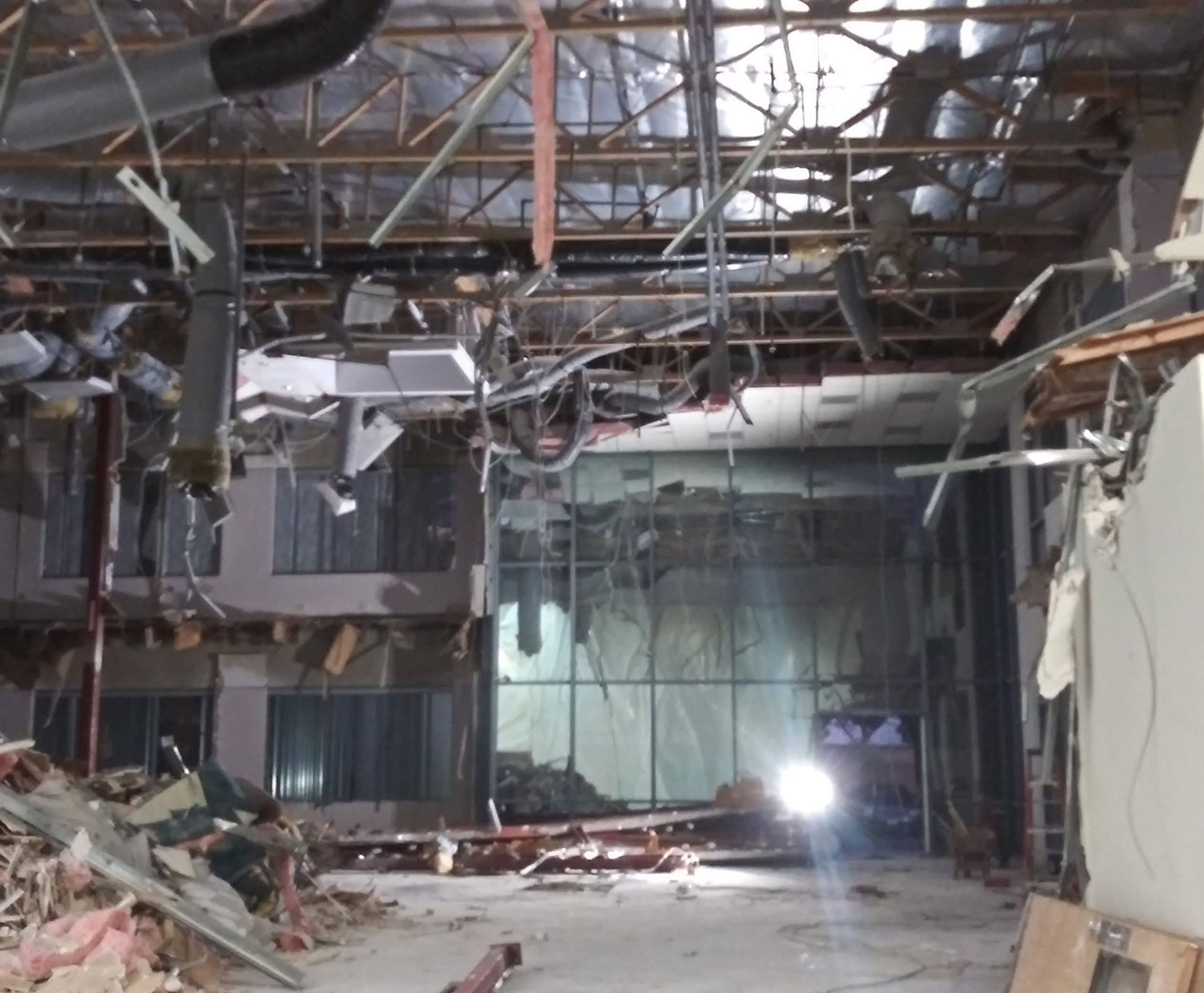 Destroyed interior with collapsed ceiling, exposed wiring, rubble, and bright light in a damaged room