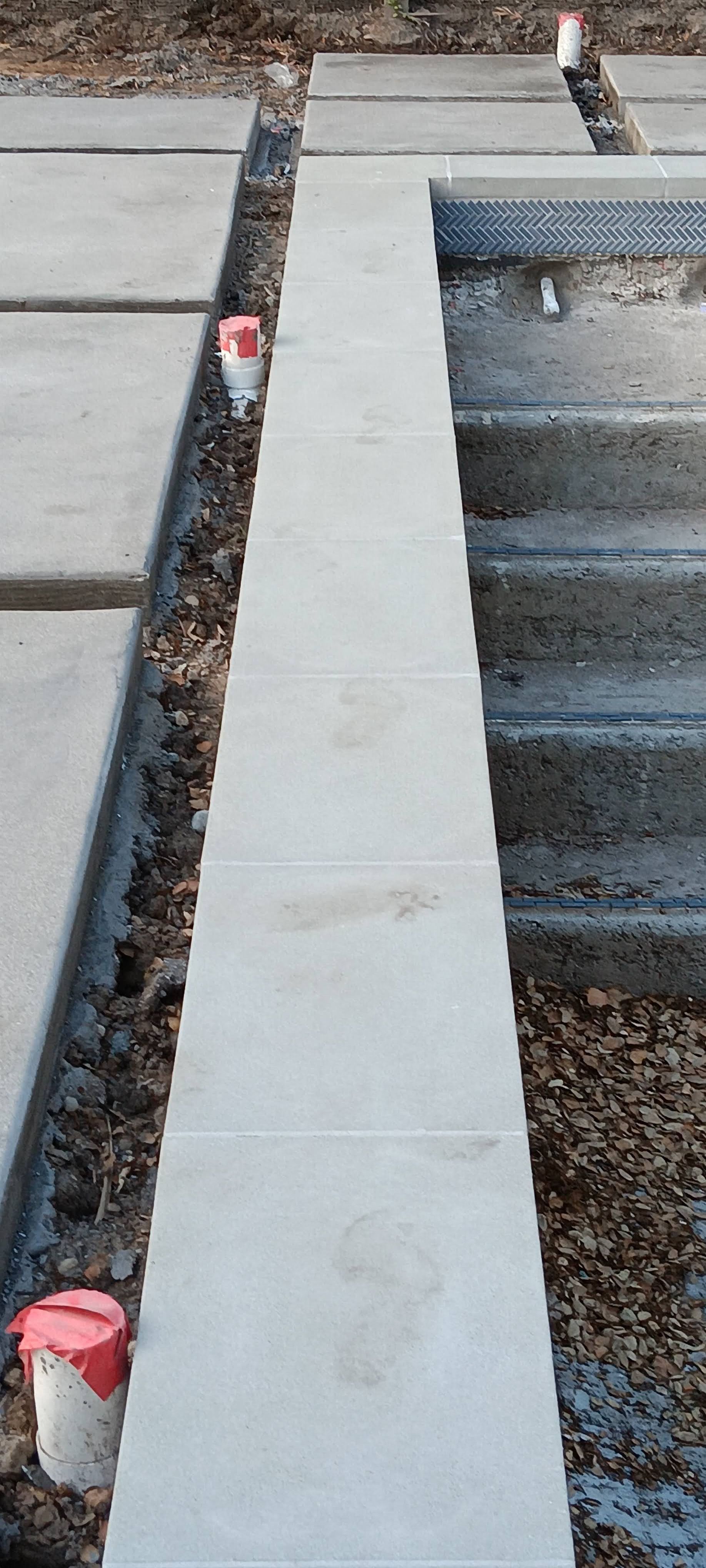 Concrete walkway beside steps with red-topped markers in gravel-lined gaps