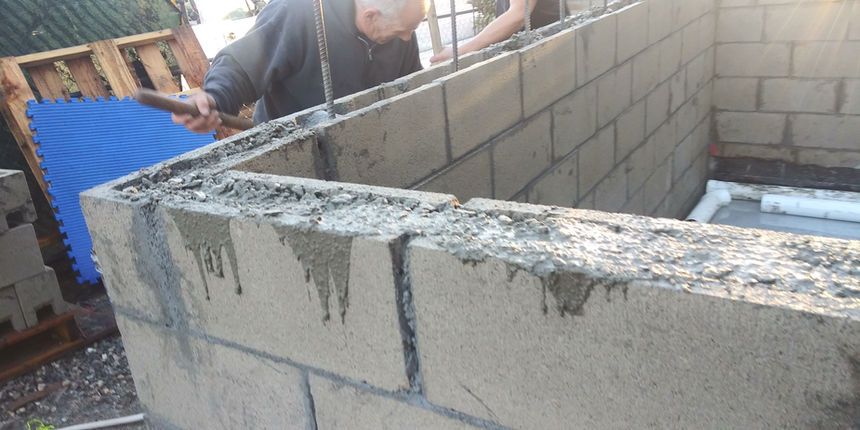 Person building a cinder block wall at a construction site with wet mortar on top