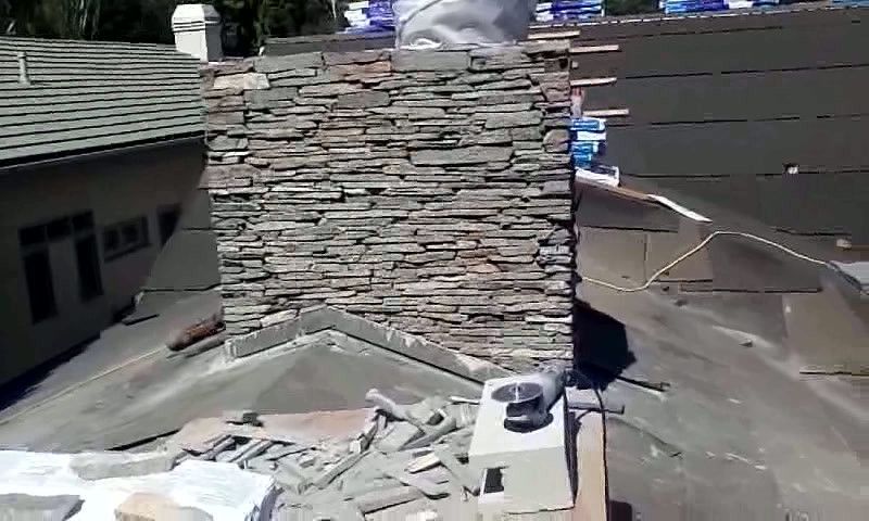 Rooftop with a stone chimney being repaired amid shingles and construction materials